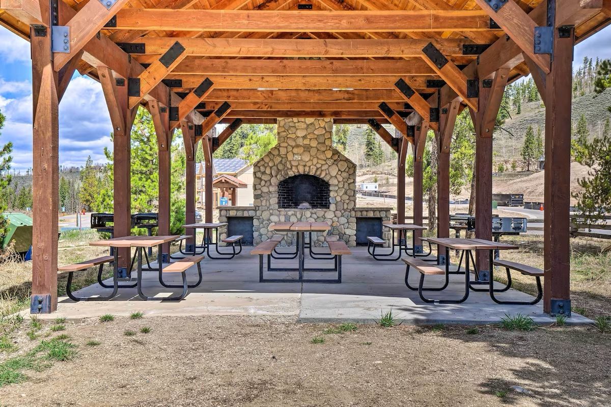 An outdoor pavilion with a stone fireplace and picnic tables.