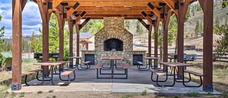 An outdoor pavilion with a stone fireplace and picnic tables.