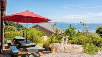 An outdoor seating area with a red umbrella, picnic tables, and a view of the water and city skyline.