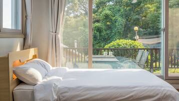 A bedroom with a large window, a bed, and a view of a balcony with outdoor furniture.