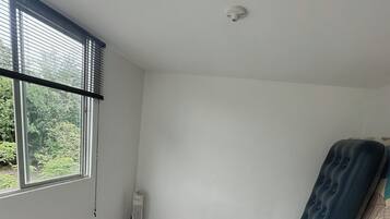 Um quarto com uma janela grande, um colchão, um armário de madeira e um piso com padrão marmorizado.