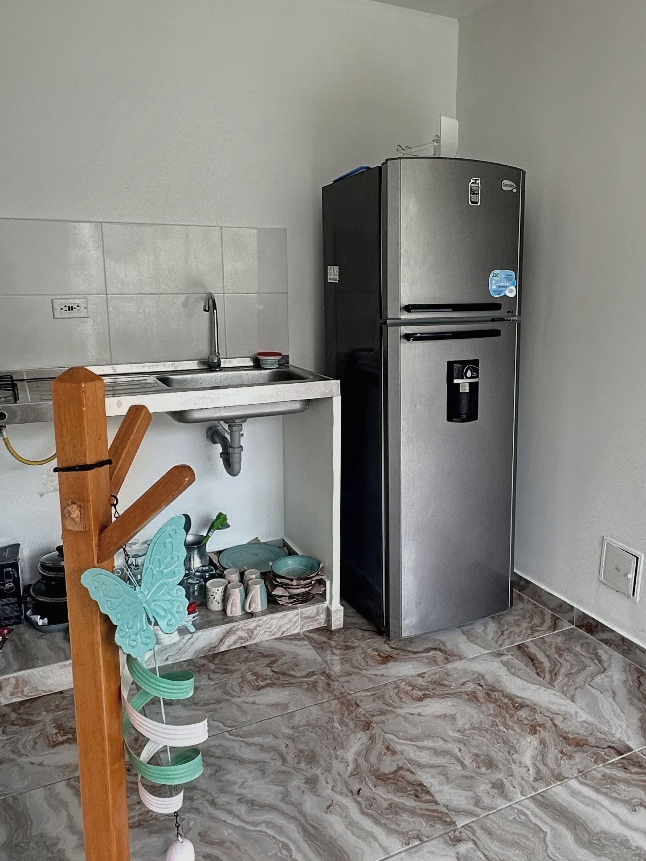 Uma cozinha com geladeira de aço inoxidável, um suporte de madeira suspenso e piso de mármore.