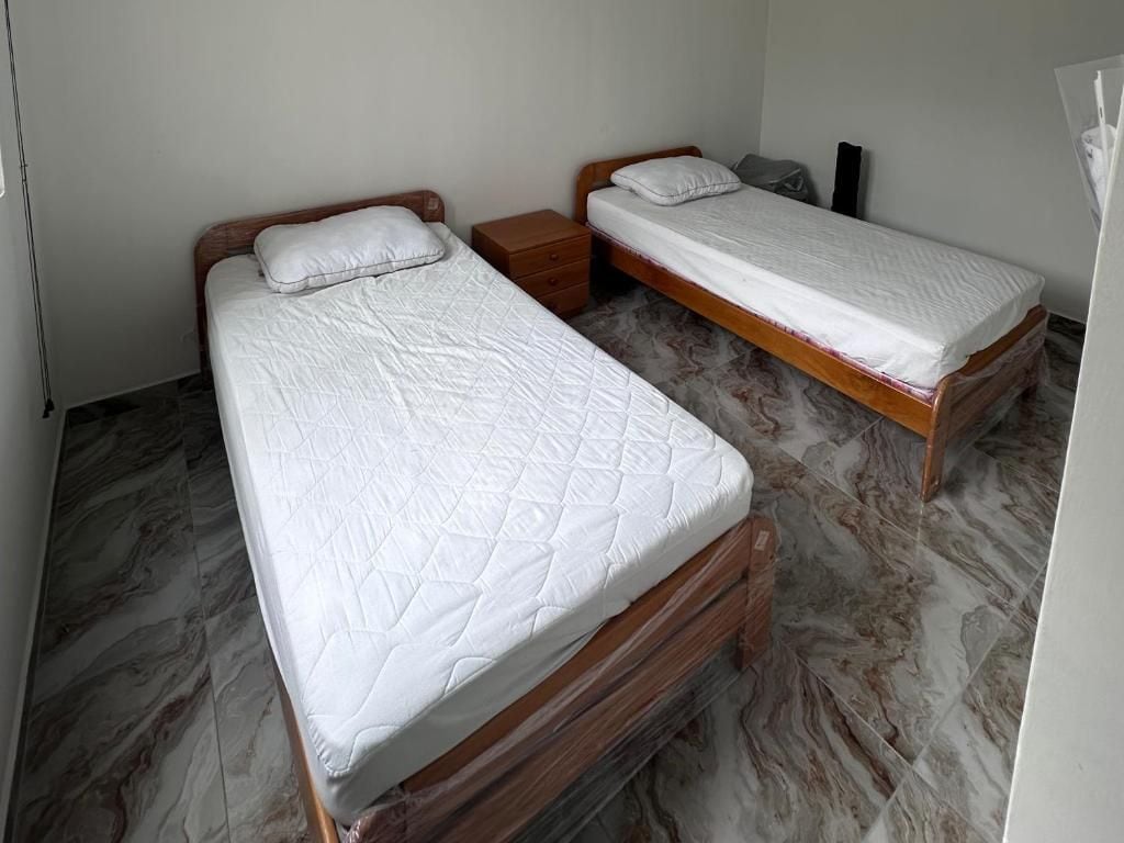 Quarto com duas camas de solteiro, cabeceiras de madeira e piso de mármore.