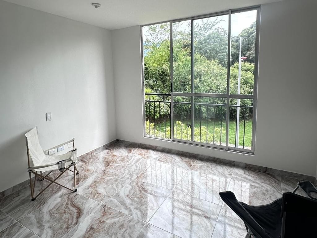 A room with a large window, a chair, and a tiled floor.