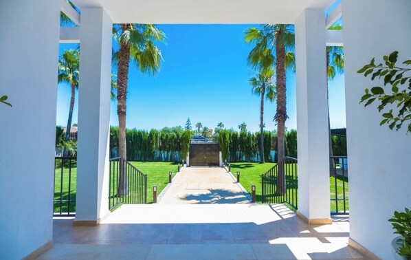 A covered outdoor area with a view of a well-maintained lawn and palm trees.