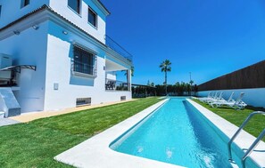 A modern building with a swimming pool, a covered patio, and a row of sun loungers.