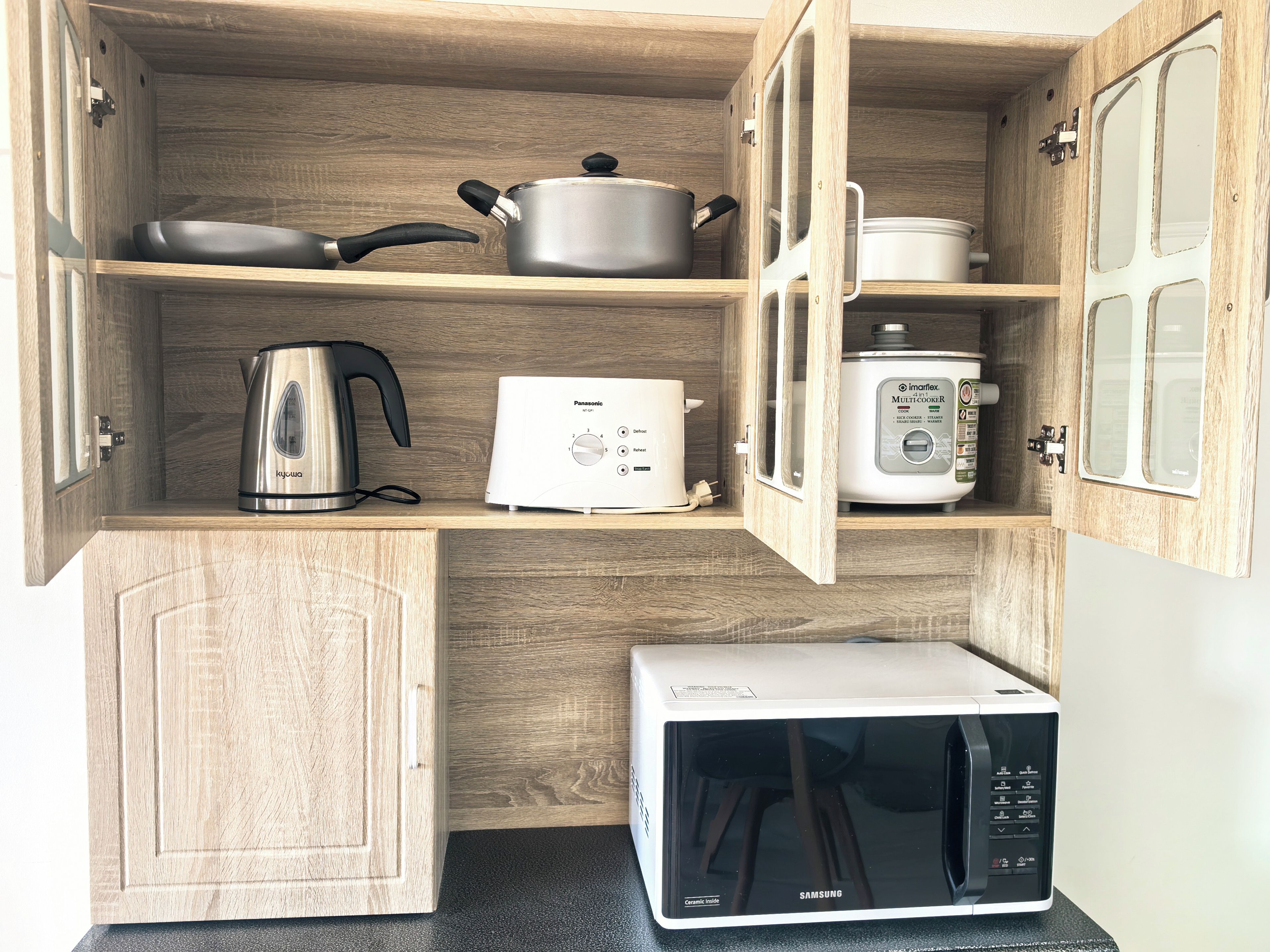 A compact kitchen with wooden cabinetry, a kettle, a toaster, a rice cooker, and a microwave.