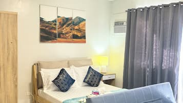 Ein modernes Schlafzimmer mit einem Bett, einem Nachttisch mit Lampe, einer Wand-Klimaanlage und einem großen Fenster mit Vorhängen.