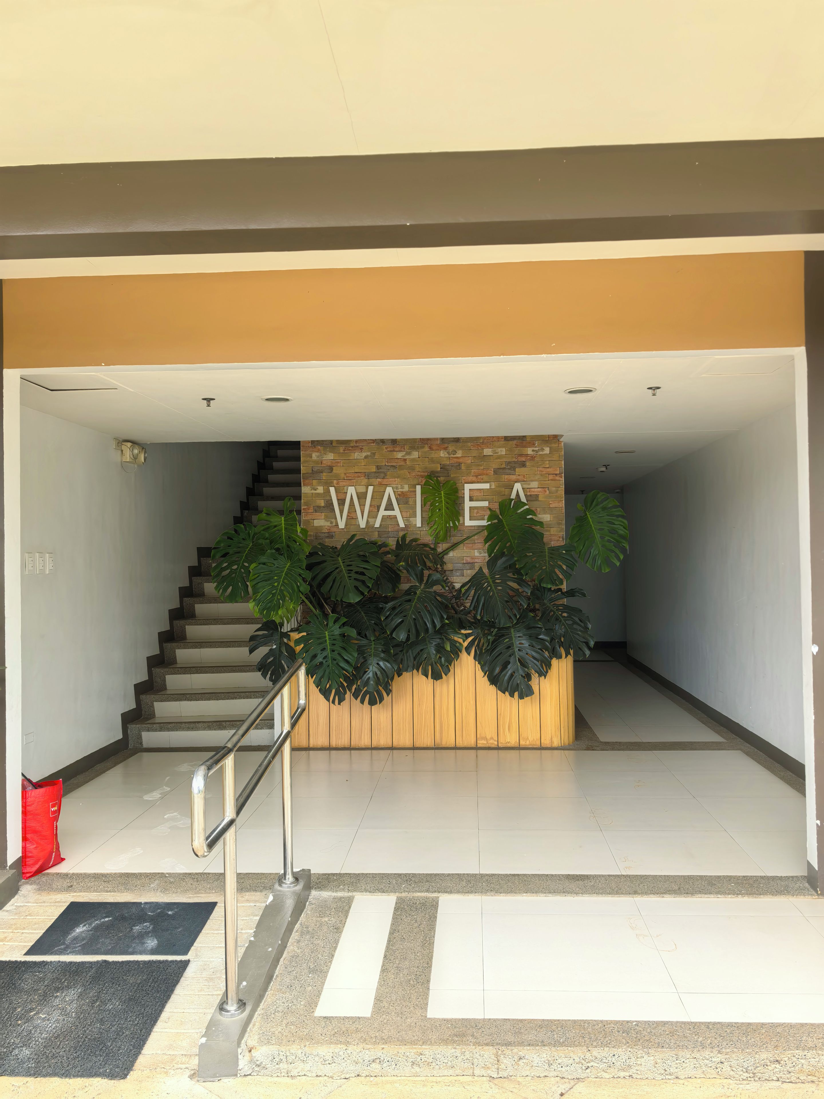 Un área de recepción con una escalera, una pared de madera con la palabra 'WAIFE' y plantas en macetas.