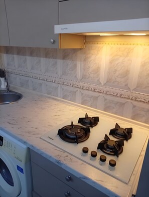 Una cocina con encimera blanca, cuatro hornillas, horno integrado y lavadora.
