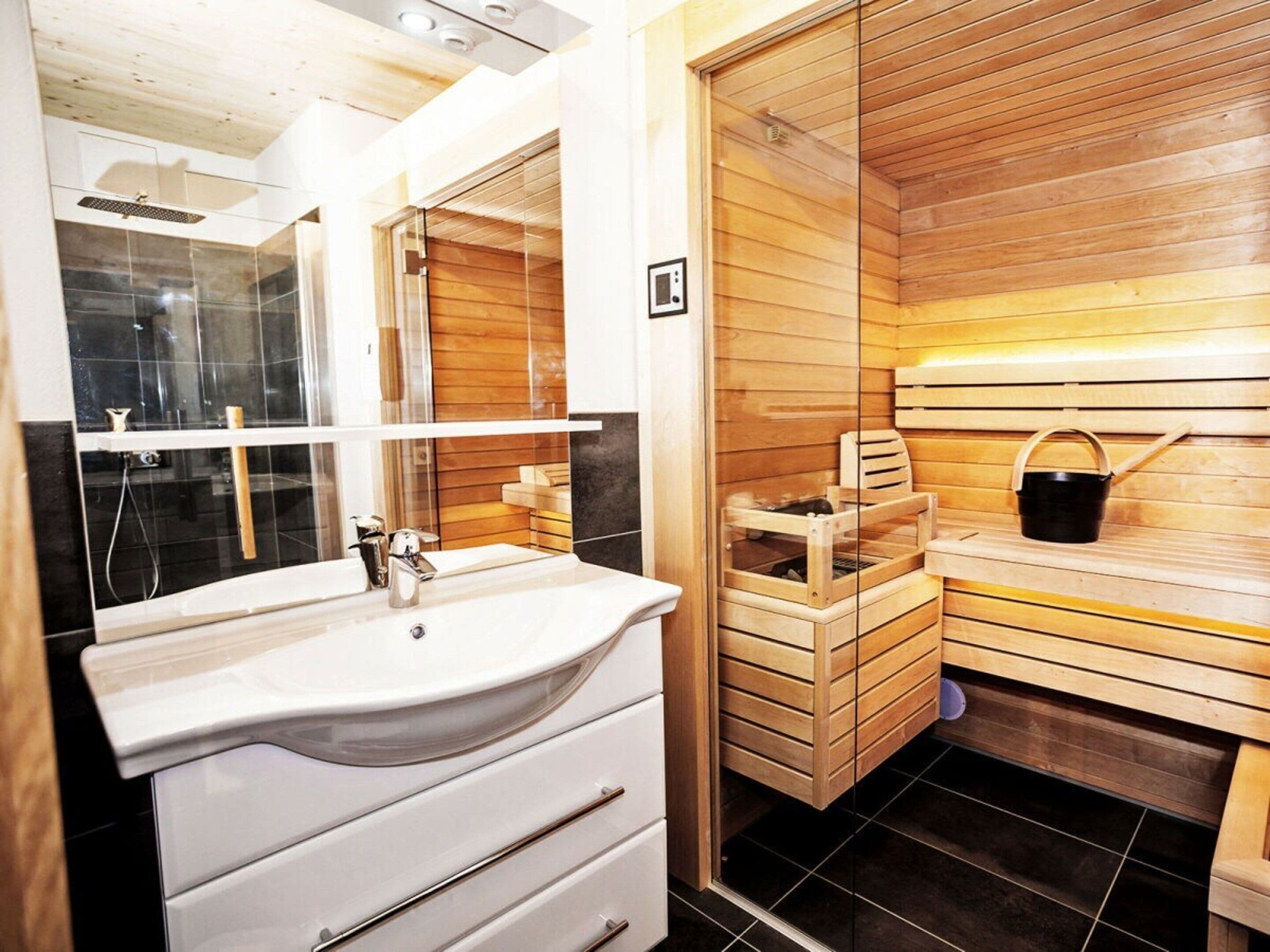 A modern bathroom with a white sink, mirror, and wooden sauna benches.