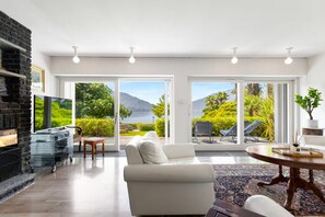 A modern living room with a fireplace, a flat-screen TV, and a large window offering a view of a mountain and greenery. - Villa on Lake Como, Relax [Parking and WiFi] (Gera Lario)