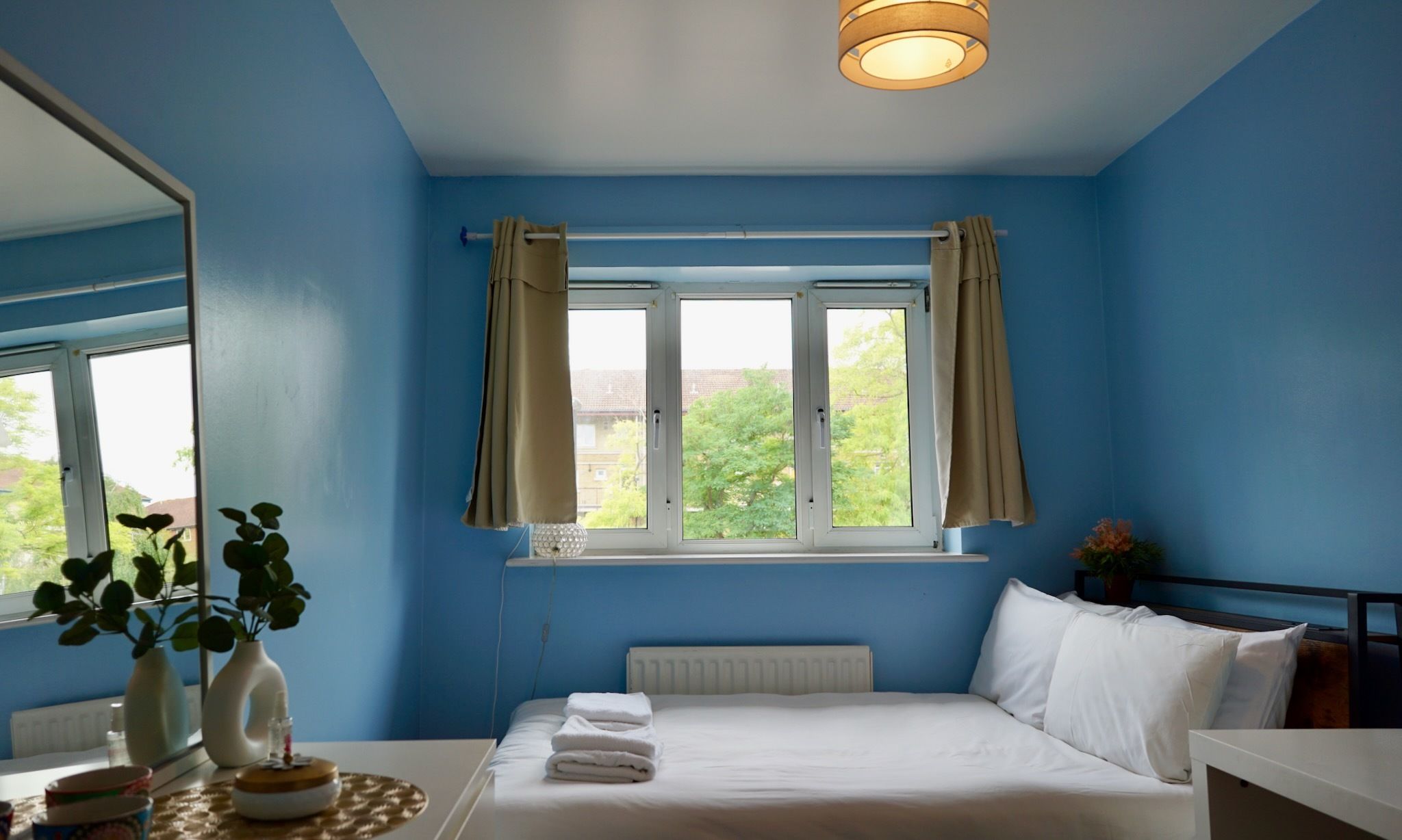 Une chambre à coucher avec un grand lit, une fenêtre avec des rideaux, un radiateur et un miroir.