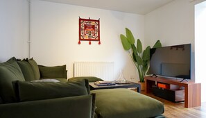 A living room with a green sofa, a white radiator, a large plant, and a television on a wooden stand. - Comfortable 2BDR 2BA Home with Garden in New Cross (Greater London)