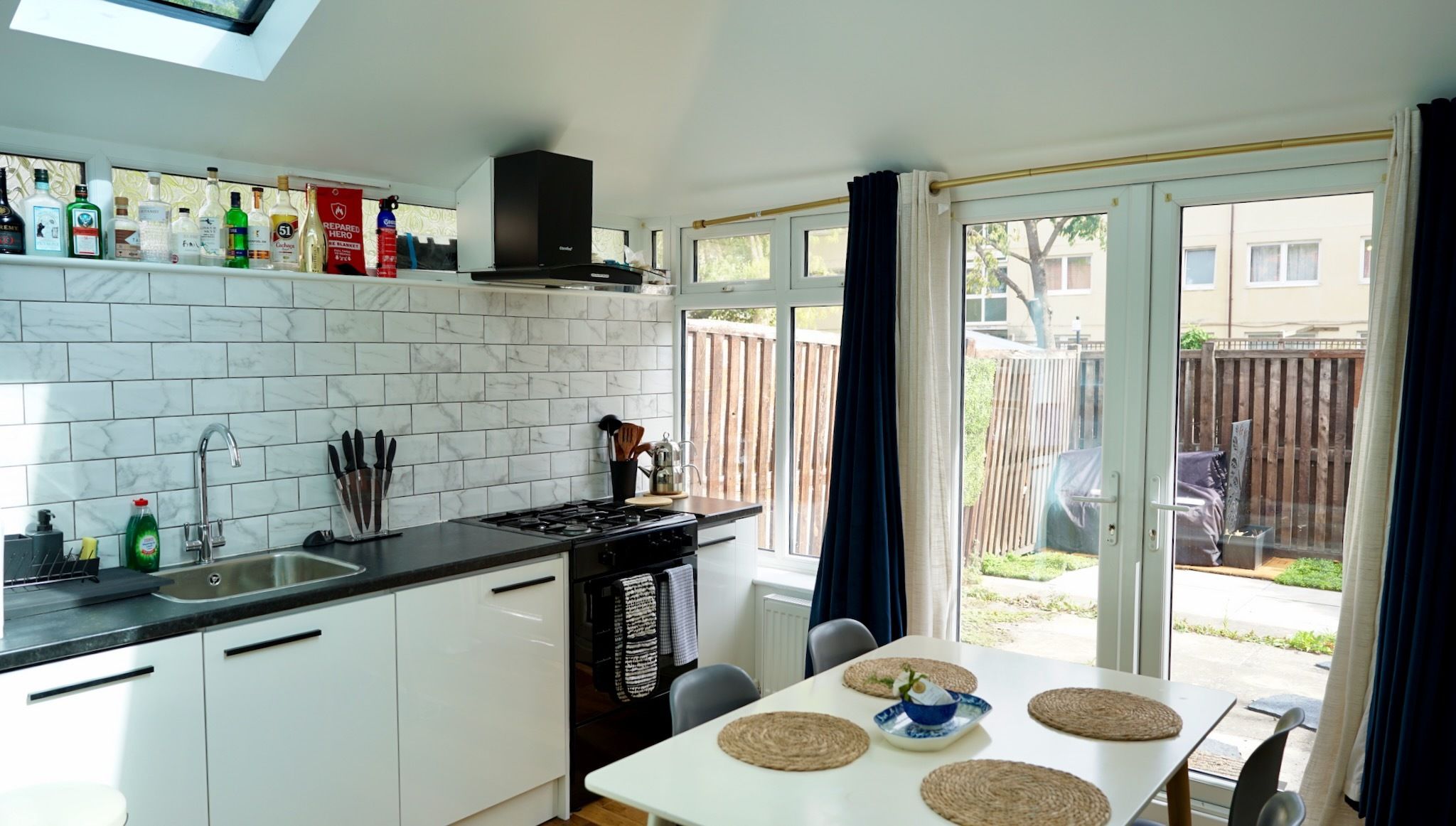 Une cuisine moderne avec des meubles blancs, une cuisinière à gaz et un coin repas avec une table dressée pour deux personnes.