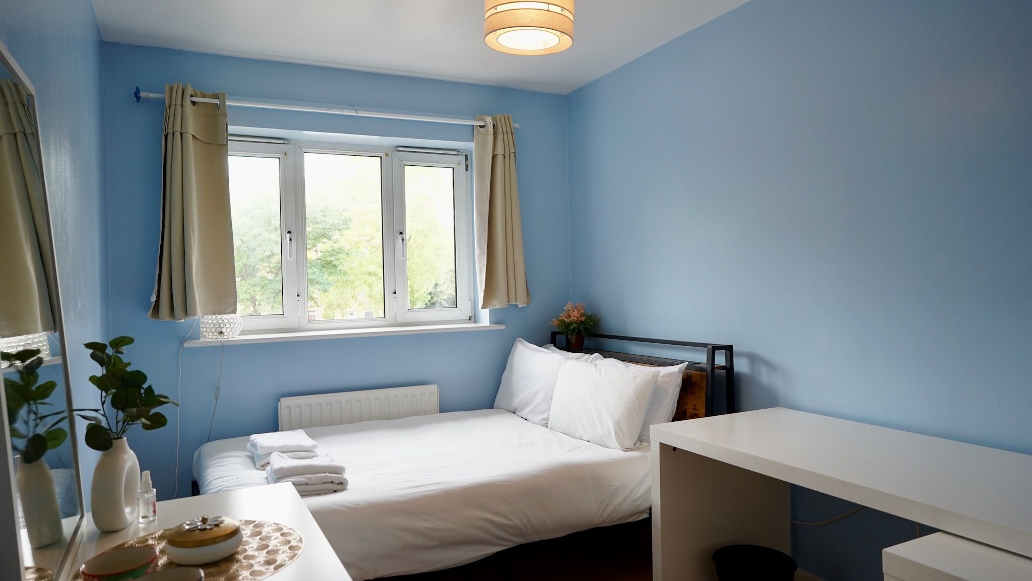 A bedroom with a bed, a desk, a radiator, and a window with curtains.