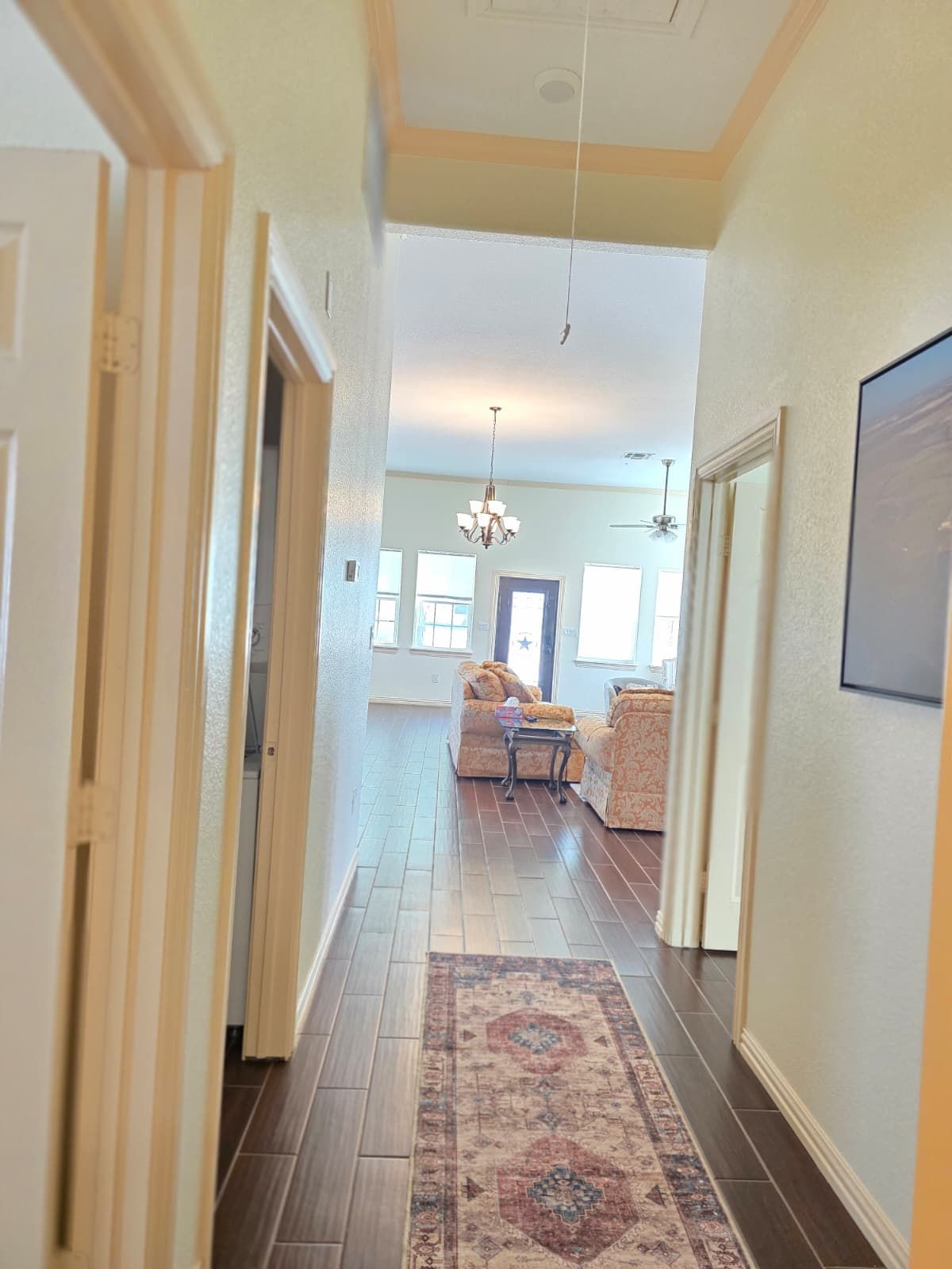 A hallway leading to a living area with a patterned rug, wooden flooring, and a ceiling fan.