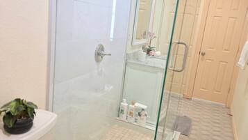 A bathroom with a glass-enclosed shower, a toilet, and a sink with toiletries.
