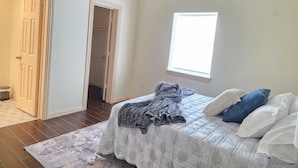 Quarto com cama, janela, porta e corredor.