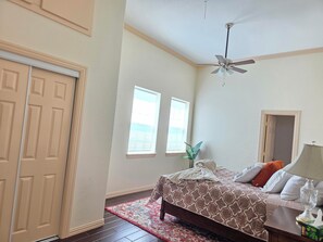 A bedroom with a bed, a ceiling fan, a window, and a door. - Serenity farmhouse (Celina)