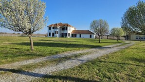 Um edifício grande e branco com telhado marrom, rodeado por grama verde e árvores.