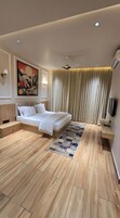 Una habitación de hotel moderna con una cama grande, piso de madera, un cuadro en la pared y un ventilador de techo.