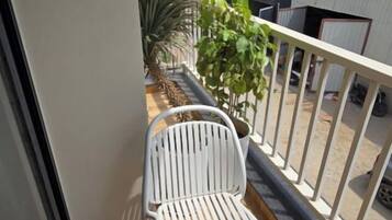 Un balcón con una silla blanca, una planta en maceta y vista de un edificio con un letrero.