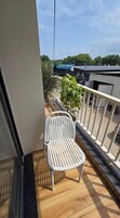 Un balcón con una silla blanca, una planta en maceta y vista de un edificio con un letrero.