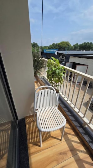 Un balcón con una silla blanca, una planta en maceta y vista de un edificio con un letrero.