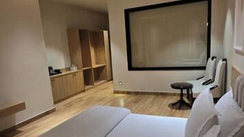 A modern hotel room with a large bed, a seating area, and a view of the city.