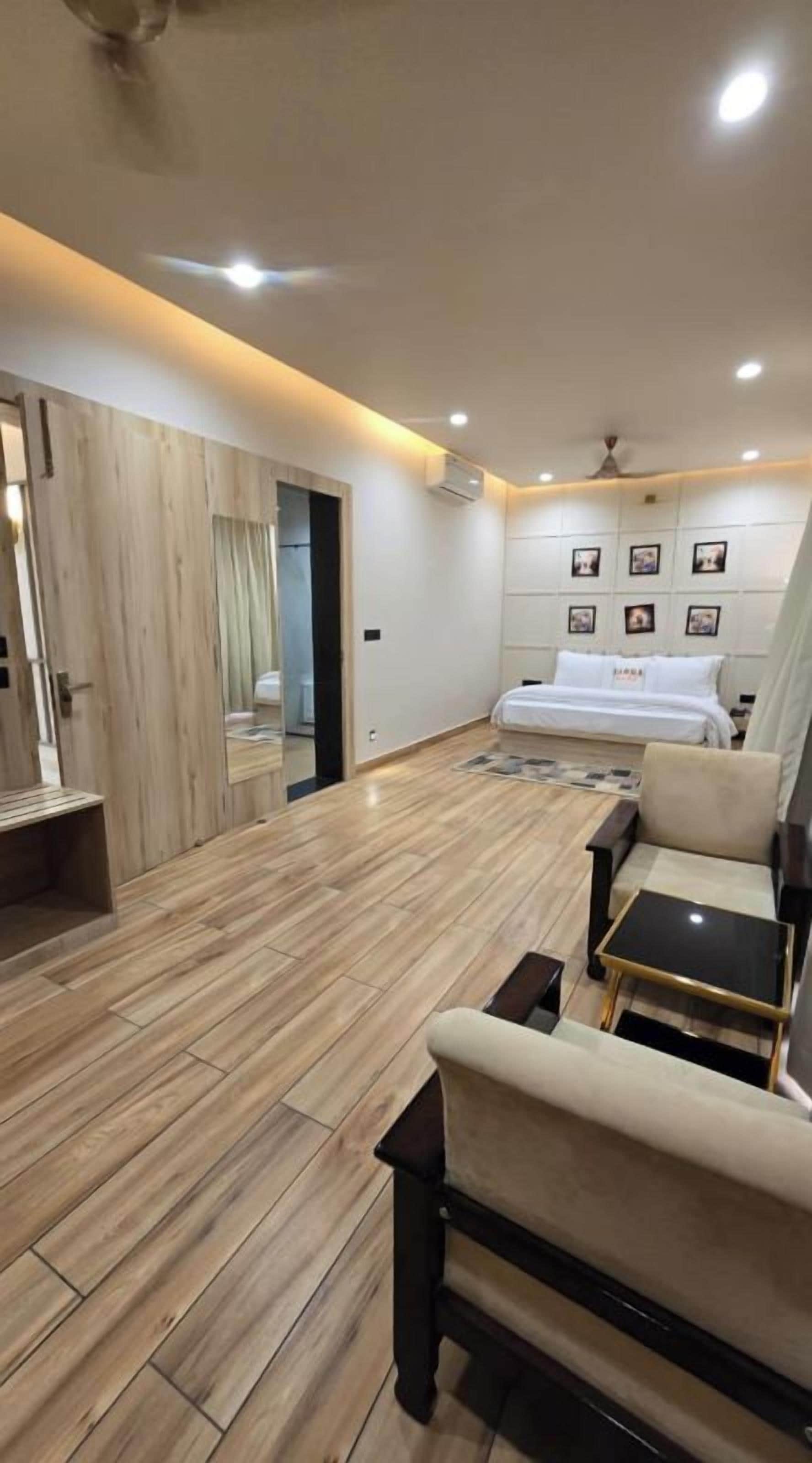 A modern bedroom with a bed, bedside tables, a seating area with a sofa and a small table, and a wooden floor.