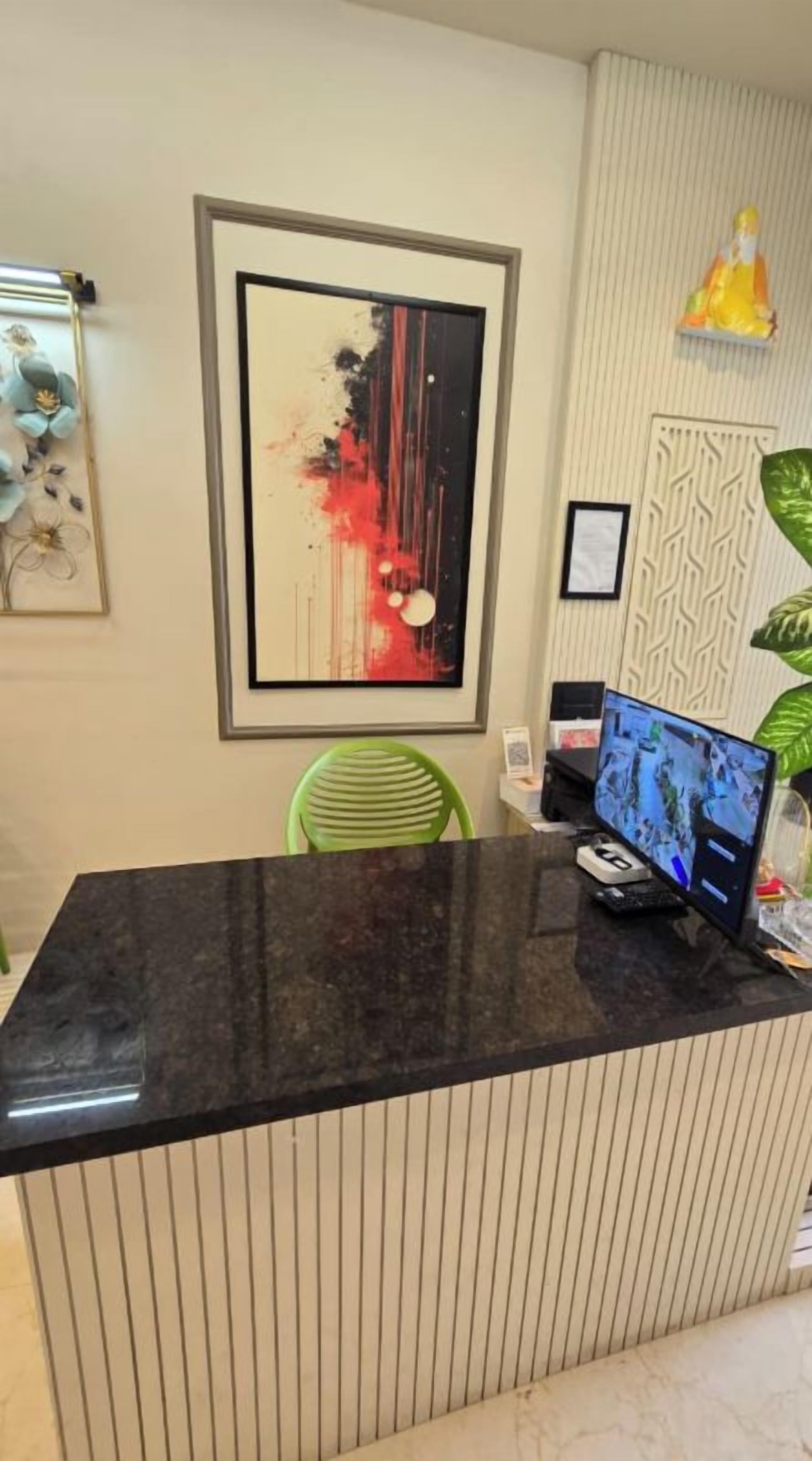 Un mostrador de recepción con un monitor de computadora, obras de arte enmarcadas y una silla verde.