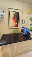 Un mostrador de recepción con un monitor de computadora, obras de arte enmarcadas y una silla verde.