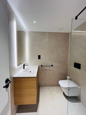 A modern bathroom with a wooden vanity, a white sink, a glass shower enclosure, and a toilet. - Fahana Residences Arguineguín (Arguineguín)