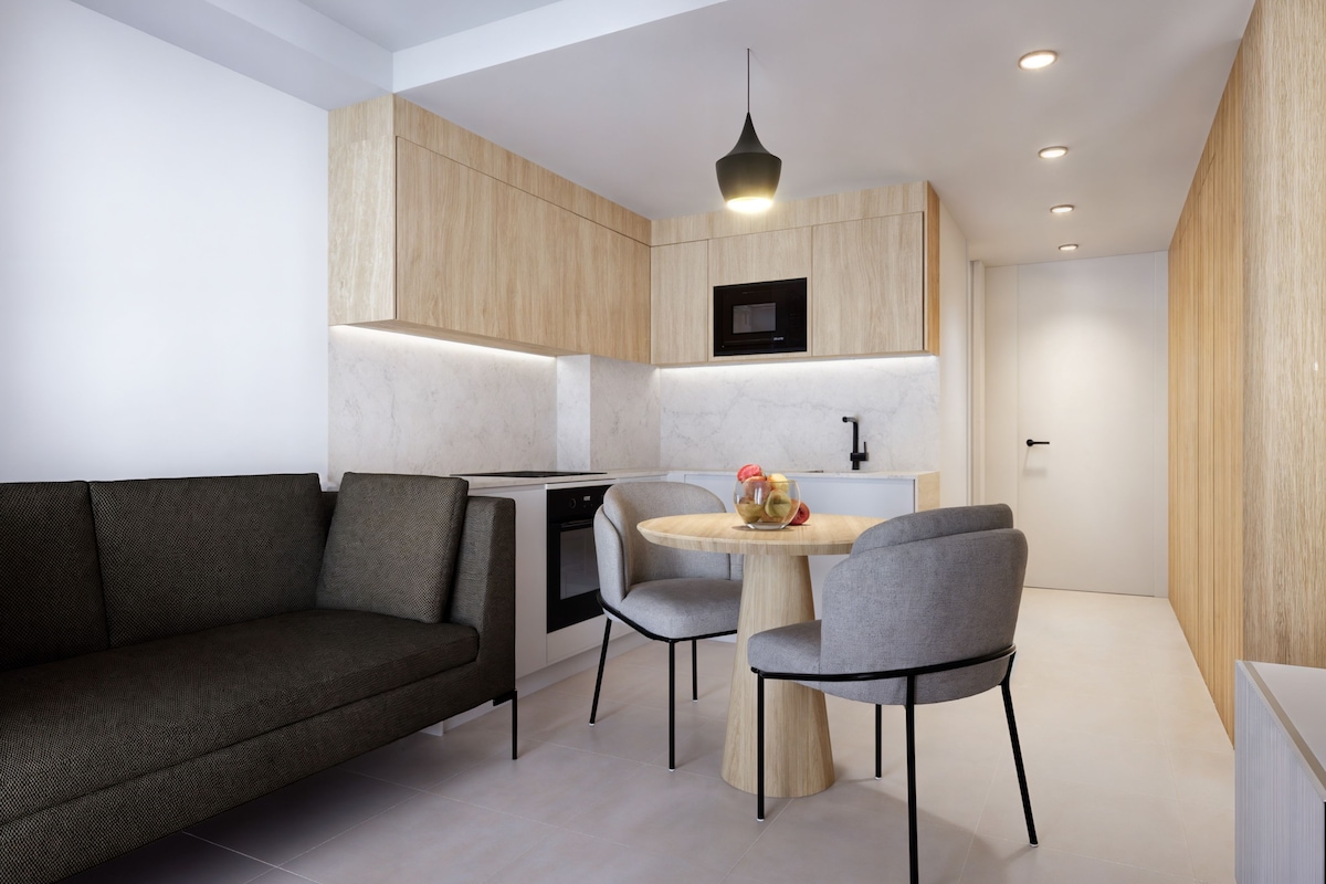 A modern kitchen with built-in appliances, a dining area with a round table and chairs, and a dark-colored sofa.