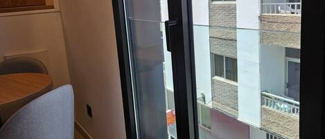A modern interior with a dining area, a large window, and a view of a building with balconies.