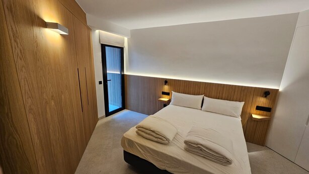 A modern hotel room with a large bed, wooden paneling, and built-in lighting. - Fahana Residences Arguineguín (Arguineguín)