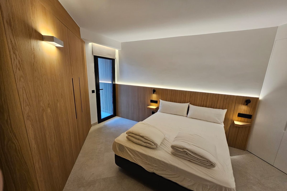 A modern hotel room with a large bed, wooden paneling, and built-in lighting.