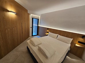 A modern bedroom with a large bed, wooden paneling, and built-in lighting. - Fahana Residences Arguineguín (Arguineguín)