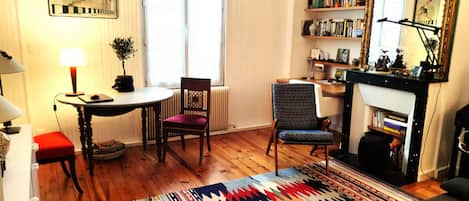 A cozy living room with a fireplace, a bookshelf, a dining area with a table and chairs, and a colorful rug.