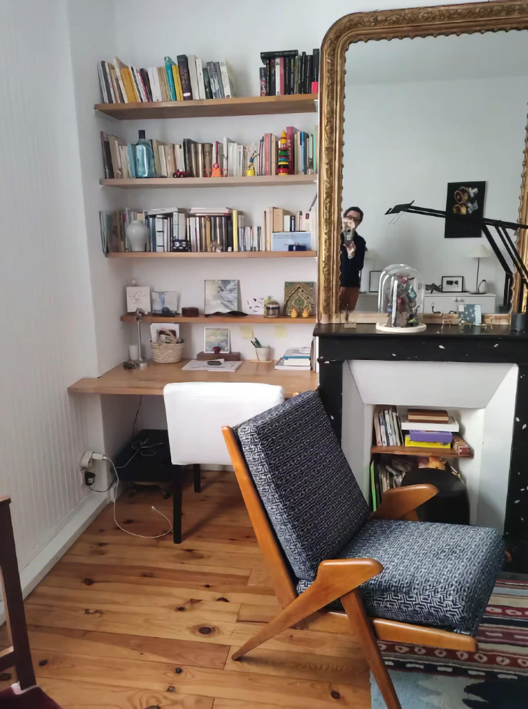Une pièce avec un plancher en bois, un bureau avec une chaise, une bibliothèque et un miroir.