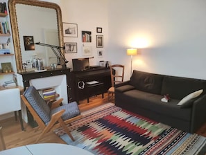 A living room with a sofa, a chair, a desk with a computer, a lamp, and a large mirror.