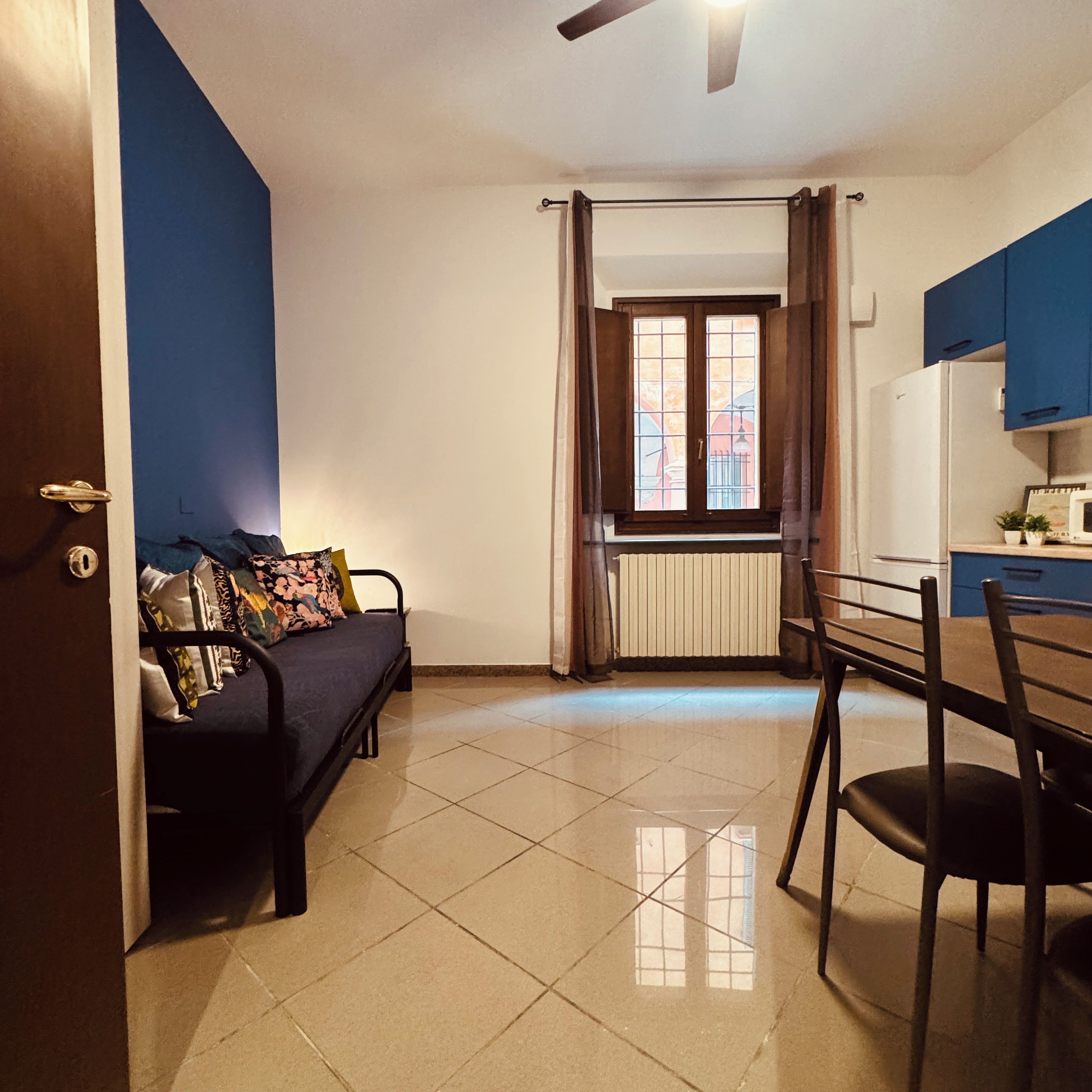 A room with a sofa, a dining table with chairs, a window with curtains, and a ceiling fan.