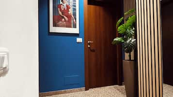 A hallway with a blue wall, a wooden door, a framed picture, a potted plant, and a light switch.