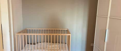 A white crib in a corner of a room with wooden flooring and a plain wall.