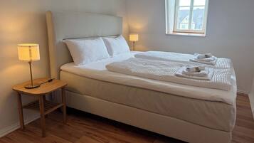 Ein ordentlich bezogenes Bett mit Kopfteil, Nachttischlampe und Handtüchern auf dem Bett.