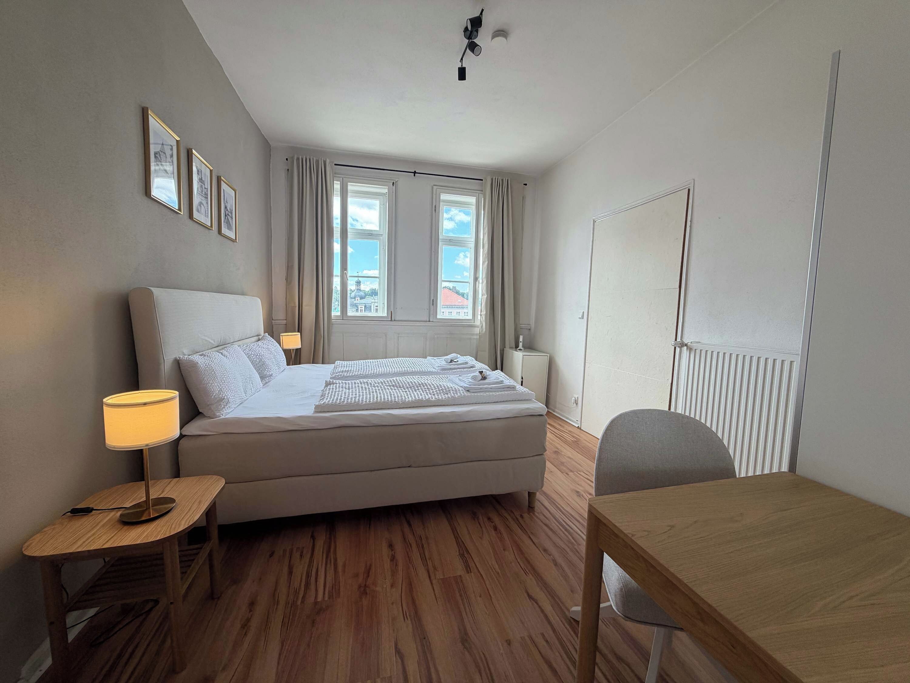 Ett hotellrum med en säng, ett sängbord, en lampa, en stol och utsikt över omgivningarna.