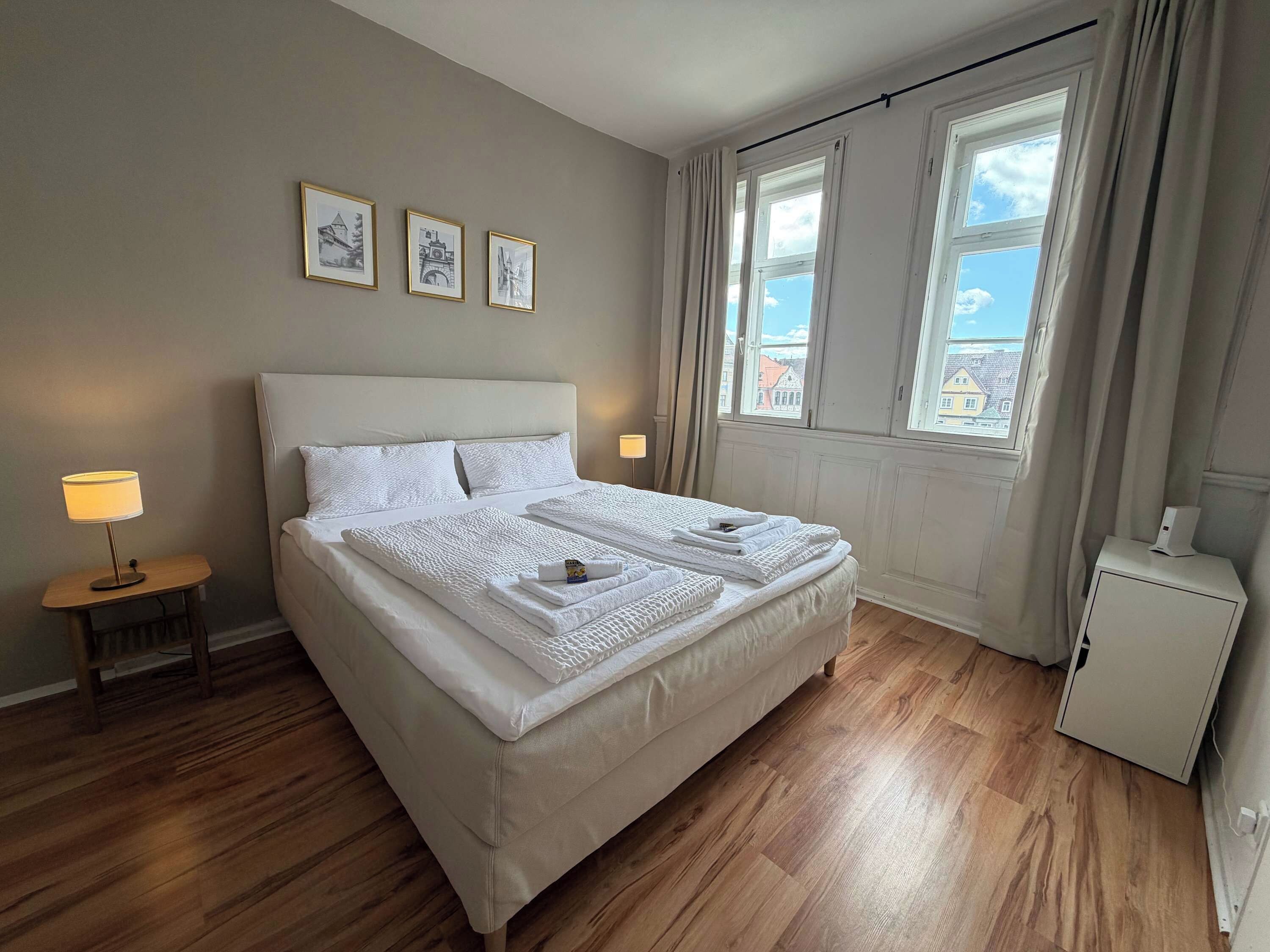 A neatly made bed with white linens, a bedside lamp, and a small bedside table.