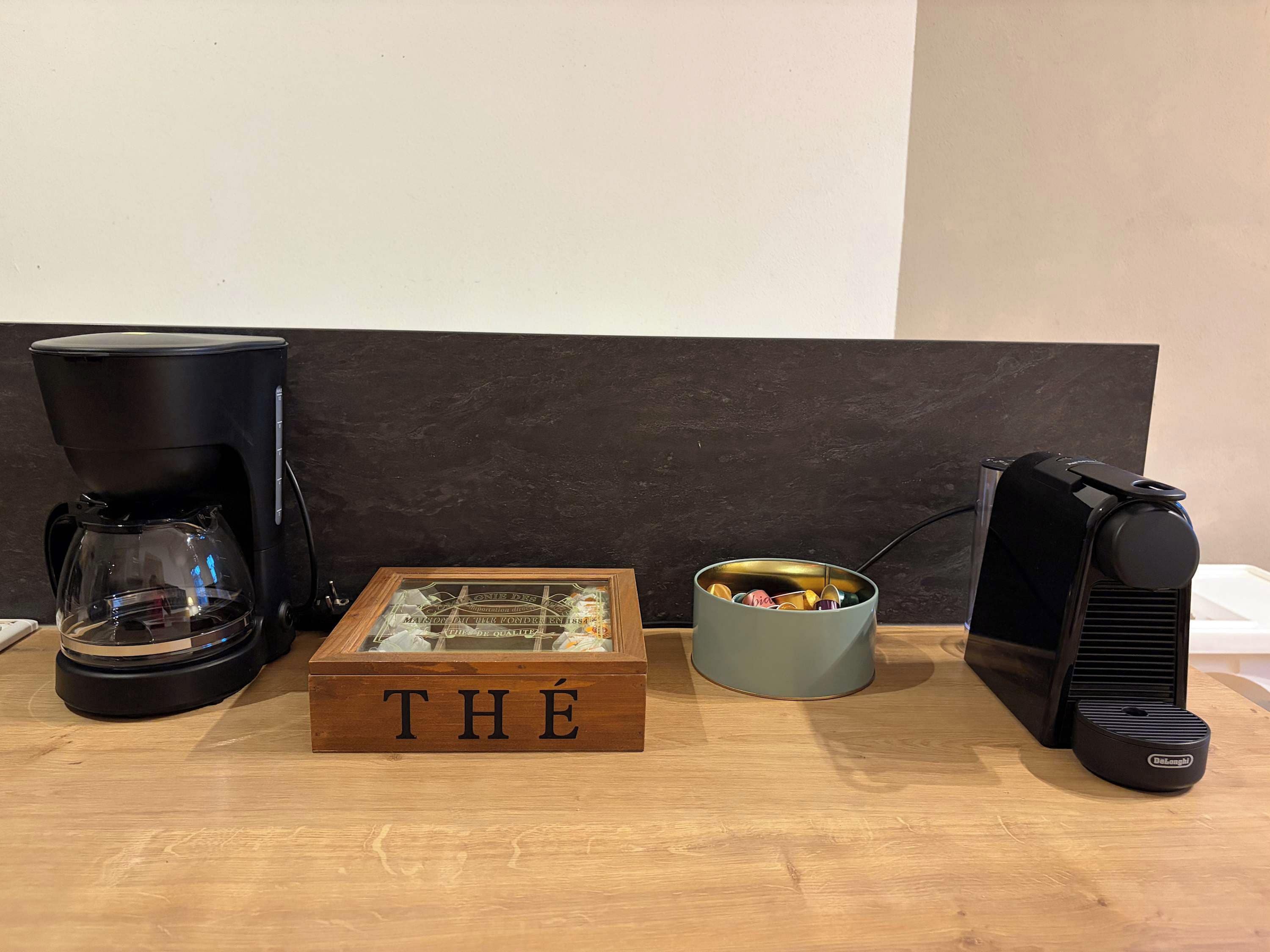 A coffee maker, a framed menu, a small container with items, and a speaker on a wooden surface.