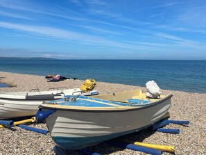 Zwei Boote an einem Kiesstrand, im Hintergrund das Meer.